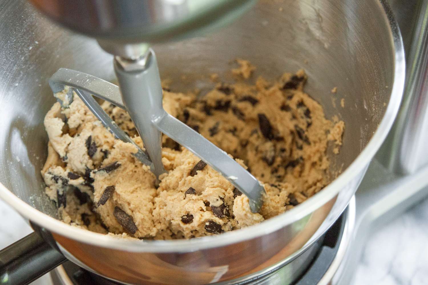 a closeup of cookie dough being mixed with a paddle attachment in the bowl of a stand mixer