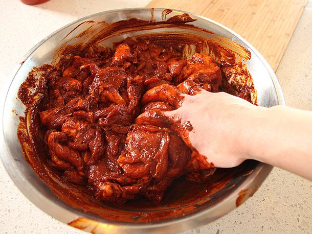 在一个大银碗里，用手将红色的卤汁混合到未煮熟的猪肉中，以确保每一片猪肉都被覆盖。