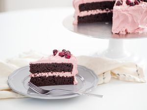 A slice of chocolate cherry layer cake is served on a grey plate. The rest of the cake is visible in the background.