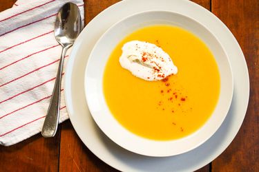 Overhead view of a white bowl of creamy spiced parsnip soup, garnished with whipped cream and cayenne.