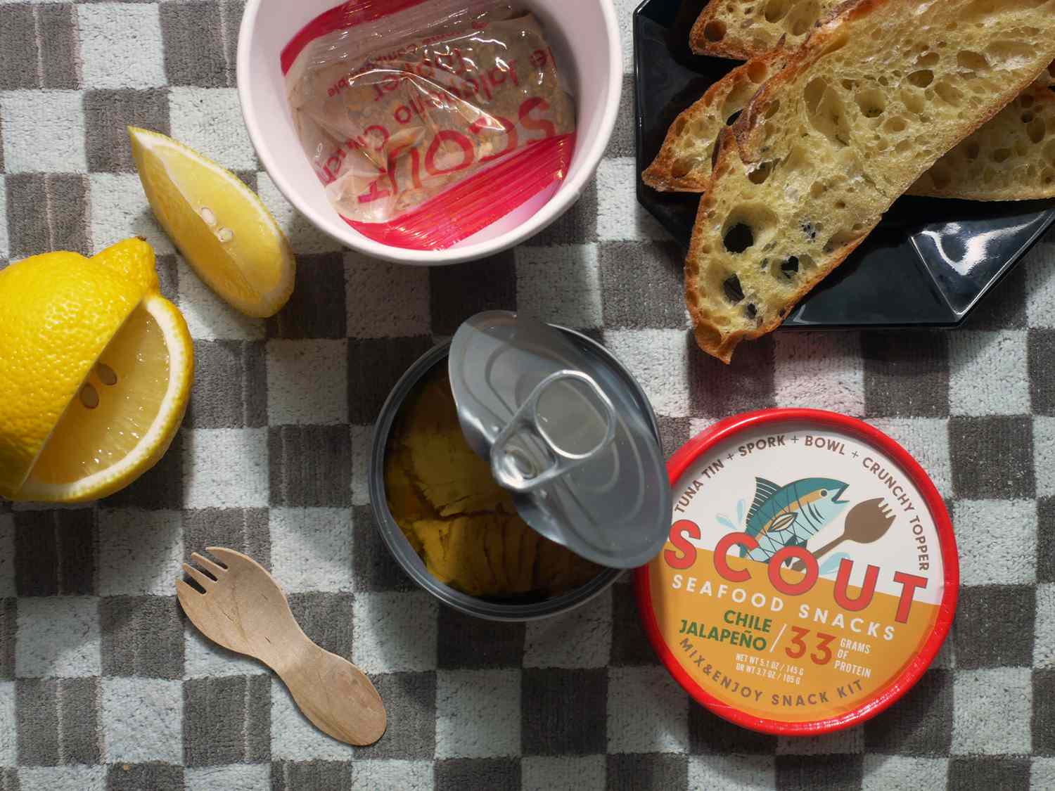 scout tinned fish cup with tin open and crisp in bag. lemon and bread on the side