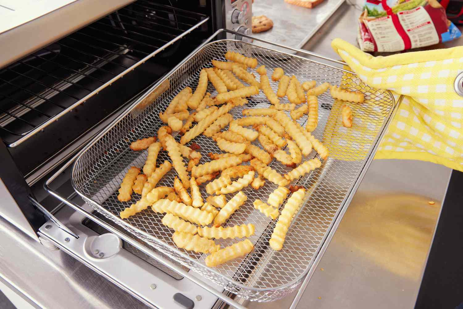 A person using a pot holder to pull out the Breville's air fryer basket that's loaded with fries