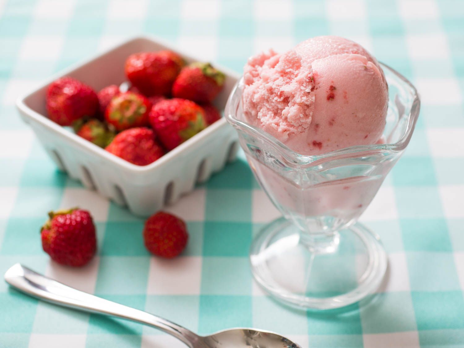 一勺草莓冰淇淋放在一个有脚的玻璃盘子里，旁边是一个草莓容器。