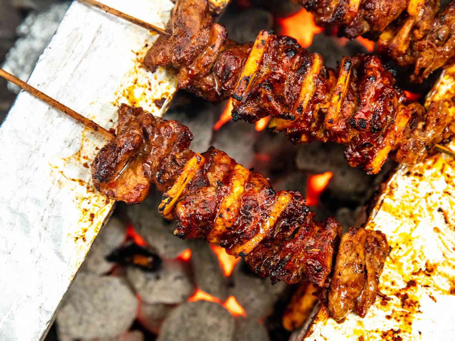 Closeup overhead shot of al pastor skewers grilling directly over hot coals.