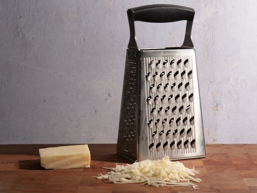 切菜板上的盒子刨丝器，两侧是奶酪皮，前景是一堆奶酪丝