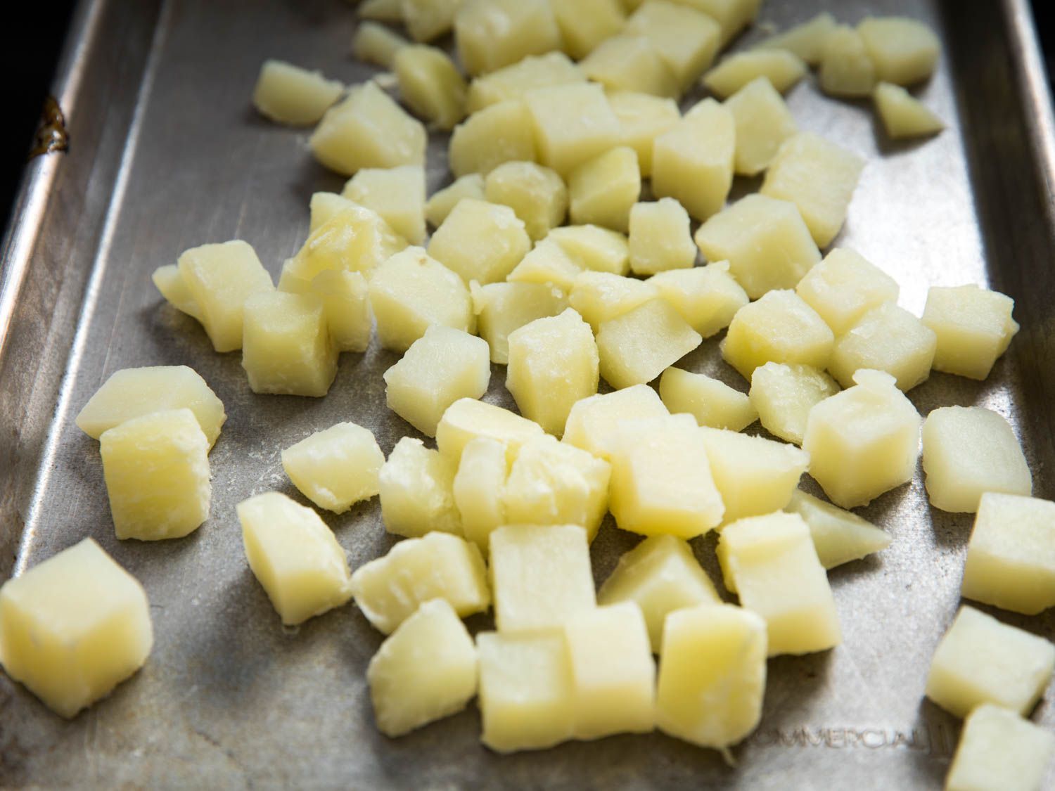Cubes of boiled potatoes spread out on baking sheet