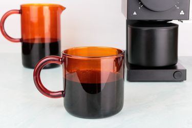 一个手动琥珀色玻璃咖啡杯，旁边是一个玻璃瓶和咖啡研磨机