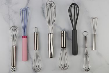 eight different miniature whisks on a marble background