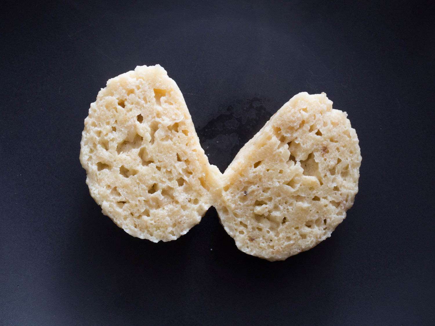Close-up of a beaten-egg-white matzo ball, cut down the middle. Both halves have been turned so that their cut side is facing the camera. The internal structure is irregular with holes and pockets.
