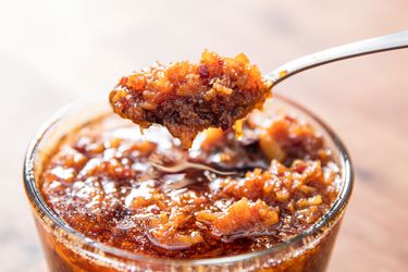 A jar of XO sauce with someone holding a spoon of sauce above the jar.