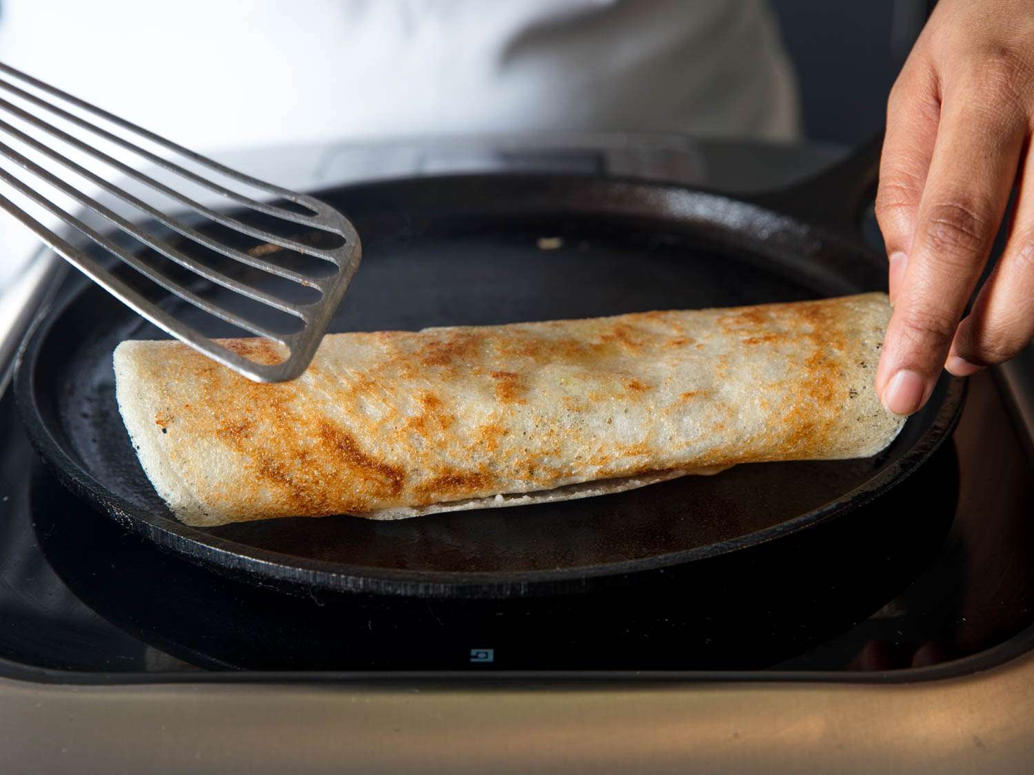 Rolling a cooked dosa on a cast iron griddle.
