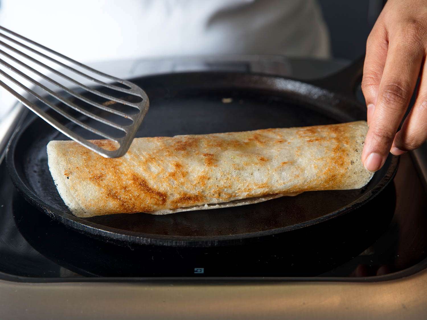 Dosa formed into a roll with a metal spatula on a plate