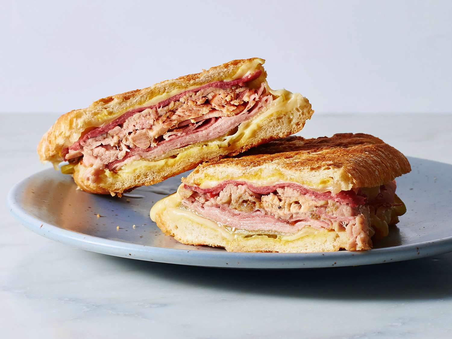 Two cut Cuban sandwiches resting on a plate.