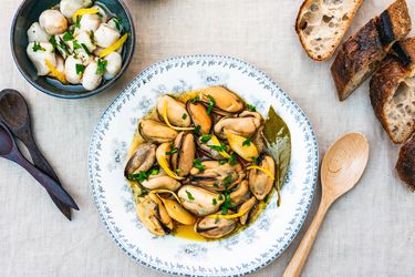 Overhead view of mussels escabeche served in a shallow bowl alongside crusty bread.