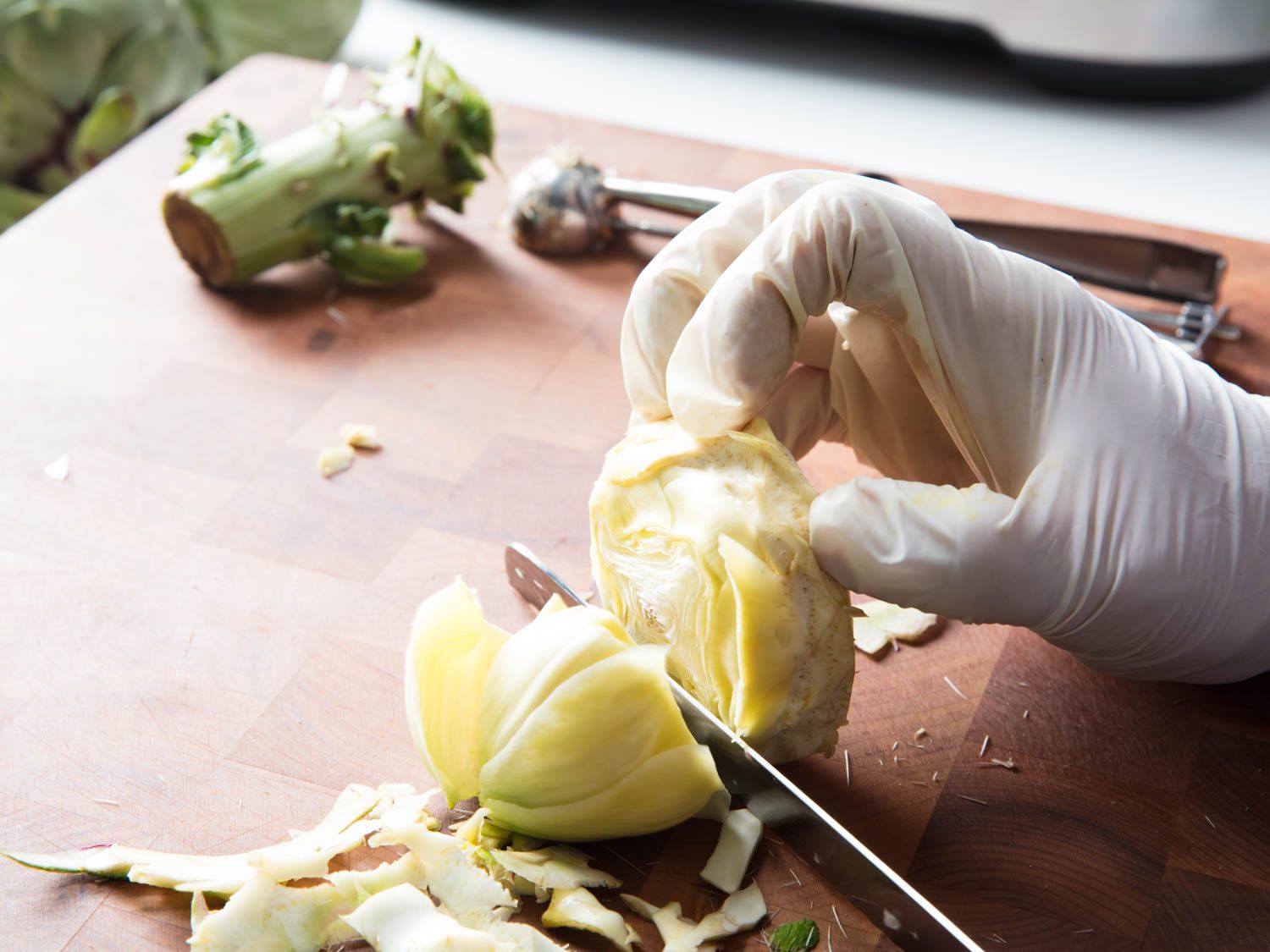 A gloved hand and a knife trimming the heart of an artichoke.