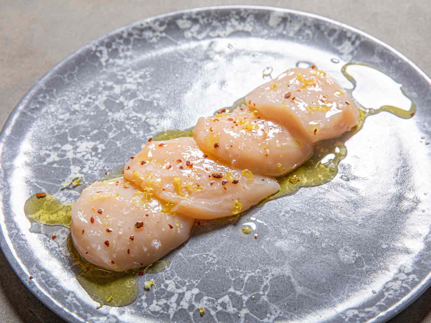 Scallop Crudo on a plate topped with olive oil and lemon zest