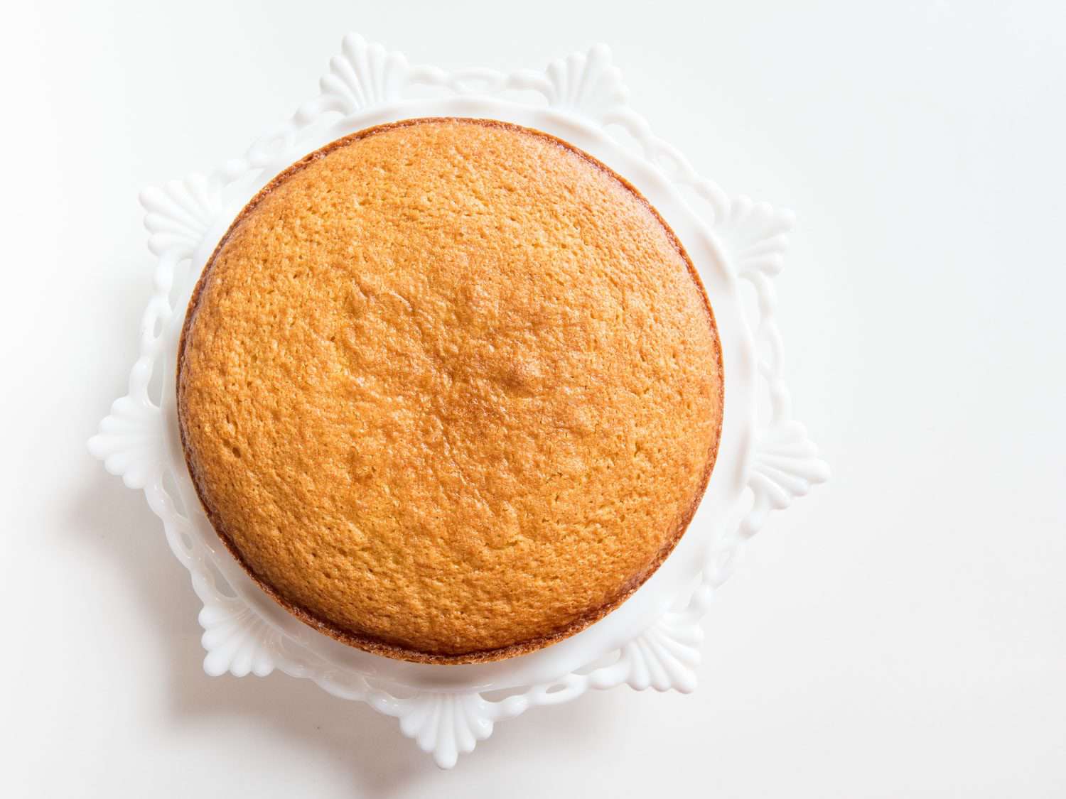 A plain, golden-brown olive oil cake on a white cake stand.