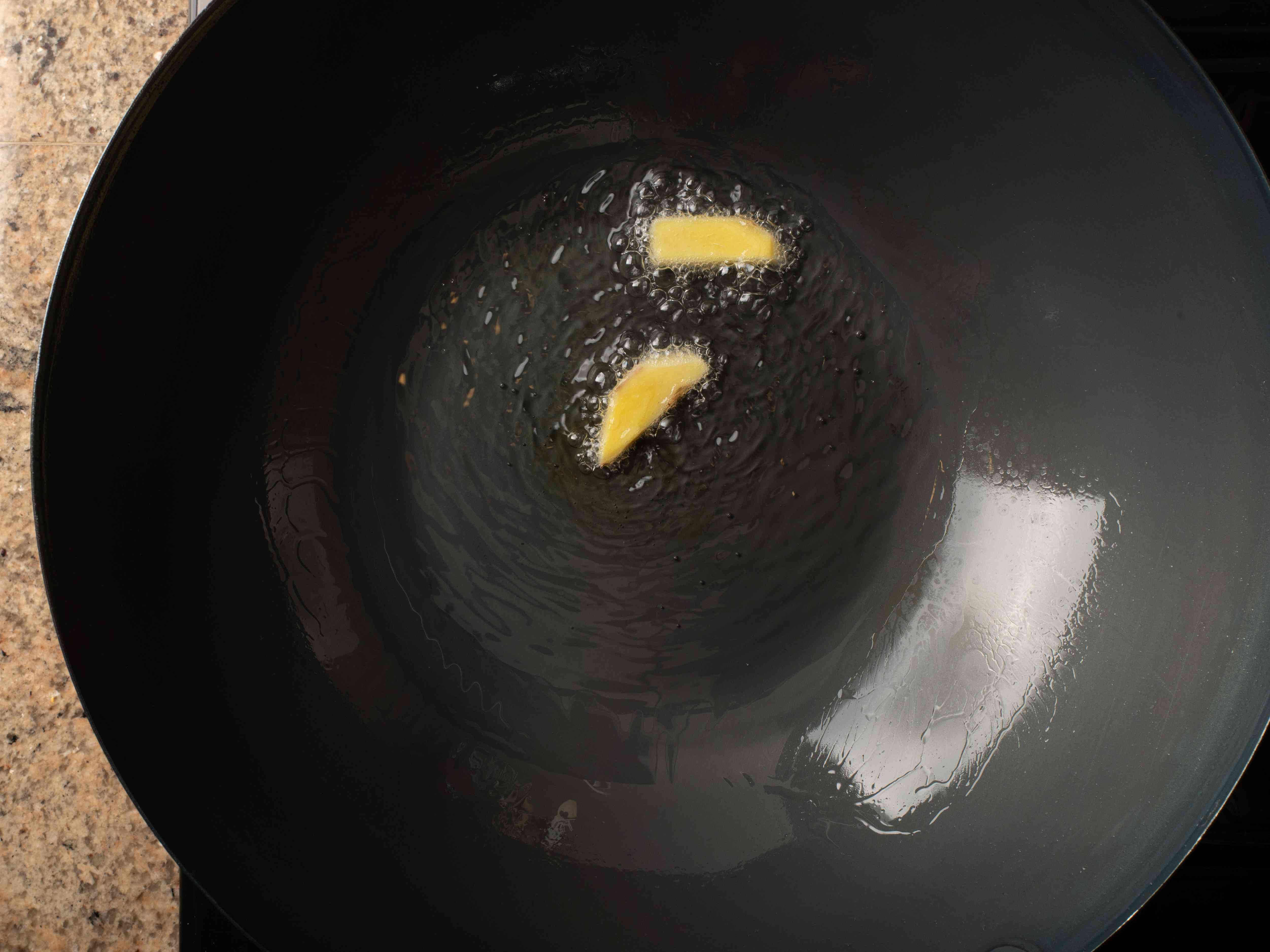 两块姜，在黑碳钢锅里放入热油。姜被小气泡包围，说明油是热的。