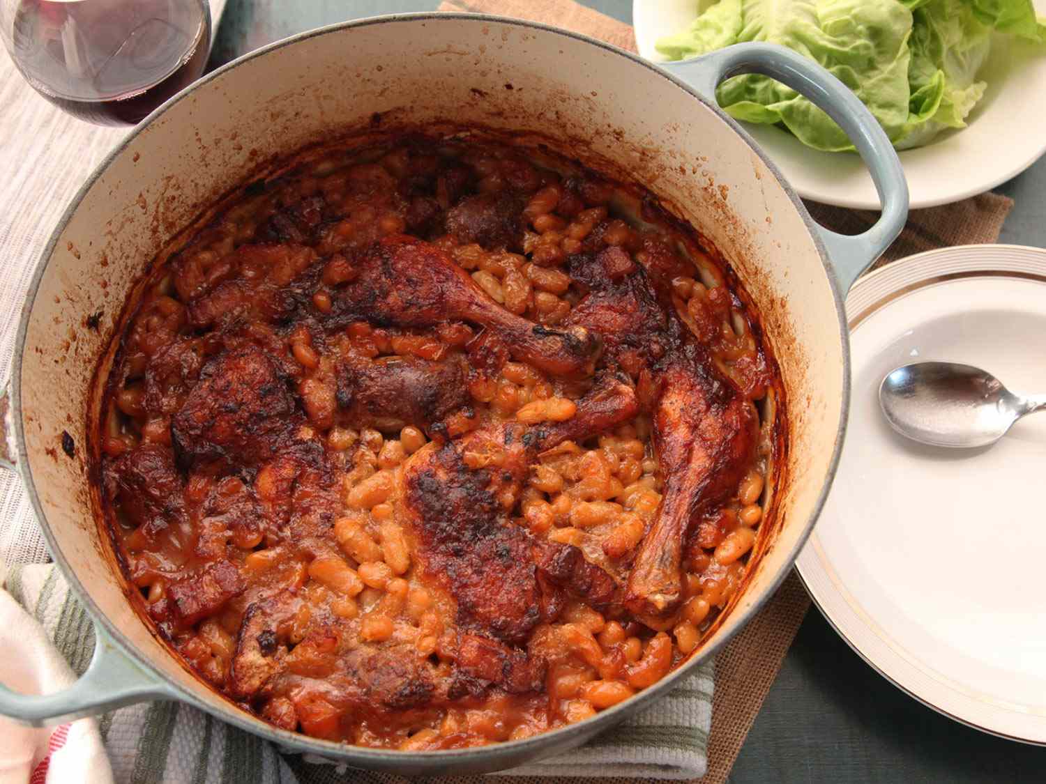 A baked cassoulet in a Dutch oven with a dry texture and crust formed by the beans and meat.