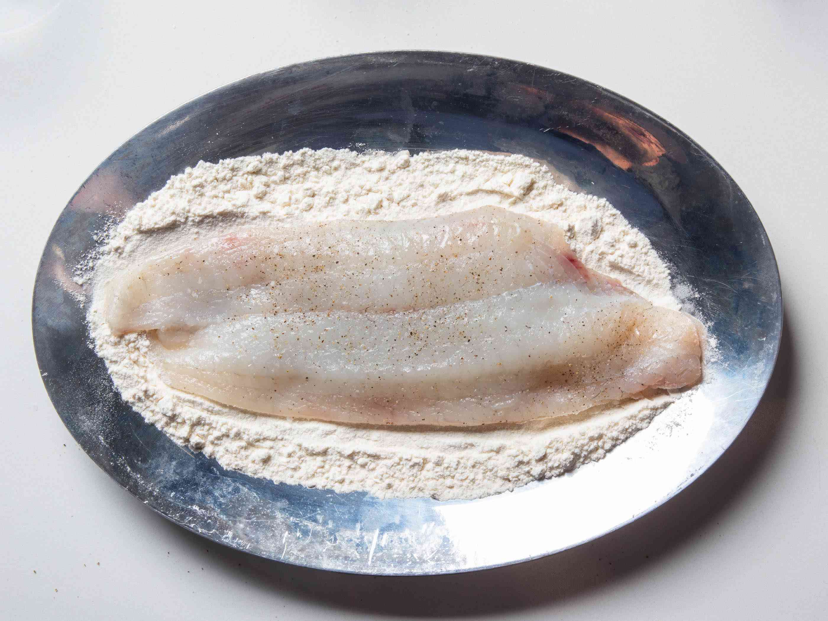 一块鲜榨黑胡椒的鱼片放在盛有面粉的圣盘里，等待疏通。