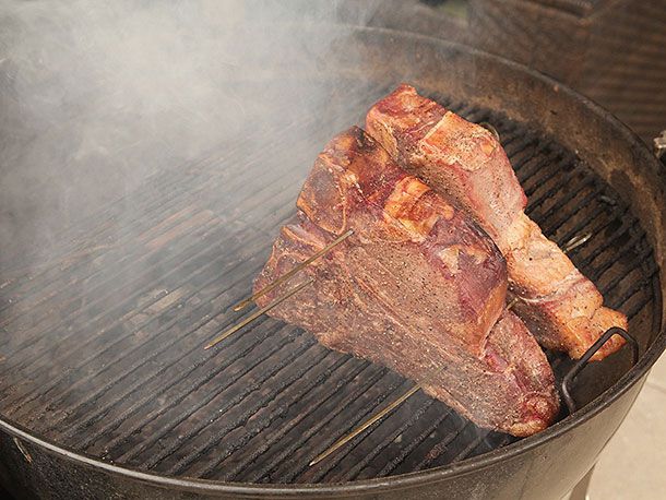 烤肉架上的上牛排，冒着浓浓的烟。牛排的表面正在变成红木色。