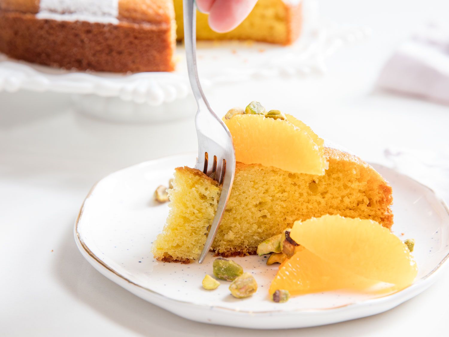 Taking a bite of golden olive oil cake garnished with orange segments and pistachios.