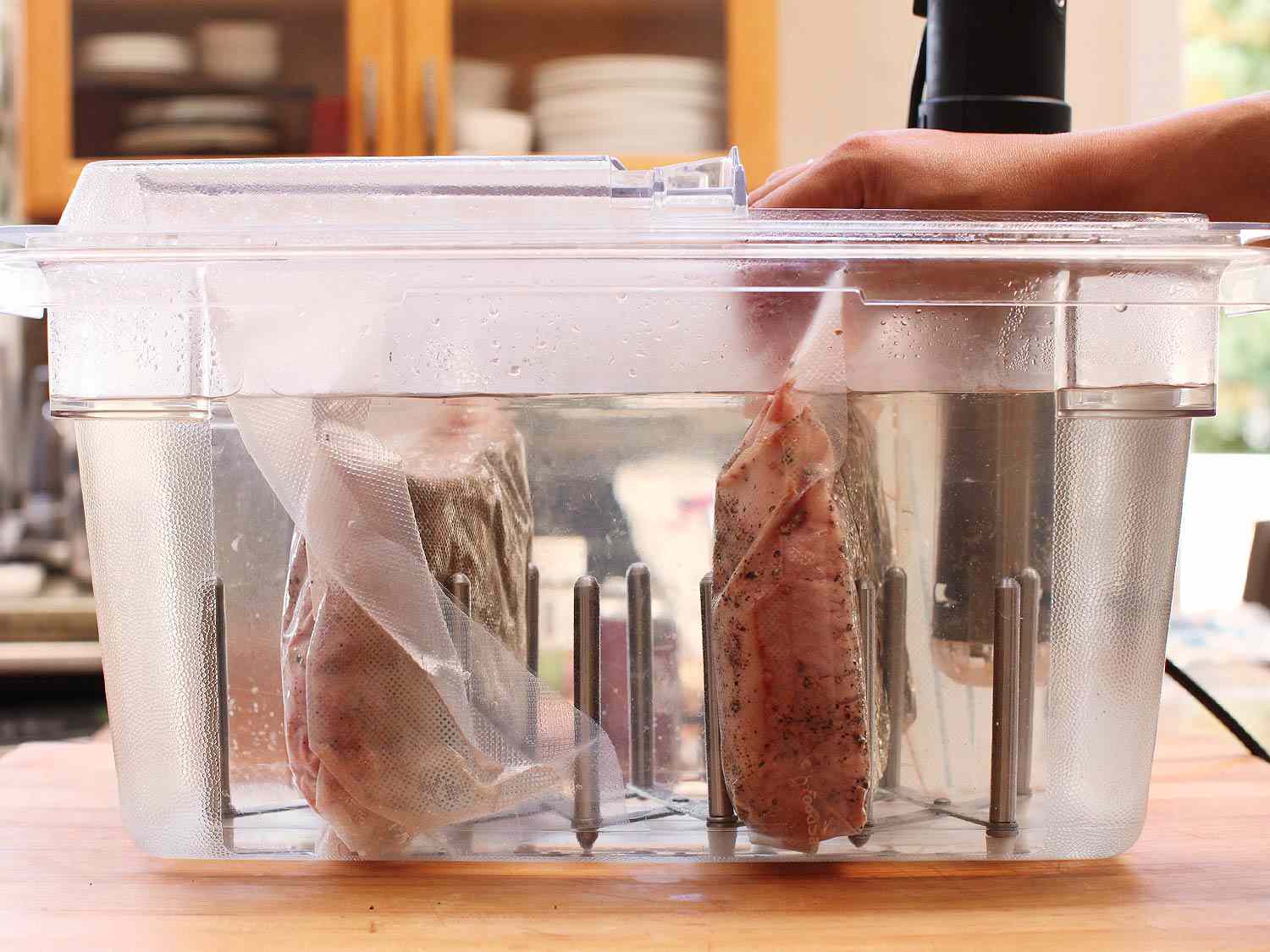 Pieces of vacuum-sealed brisket being placed into sous-vide machine.