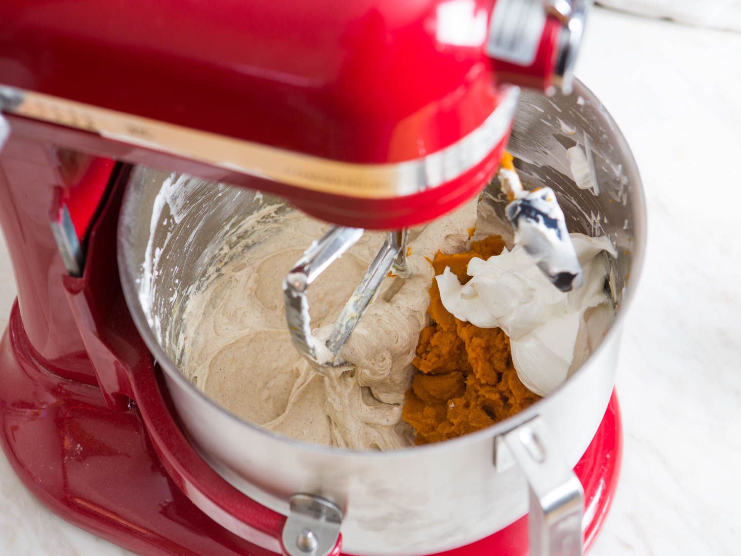 加入南瓜泥和酸奶油到搅拌碗的奶酪蛋糕混合物中，制作南瓜奶酪蛋糕。