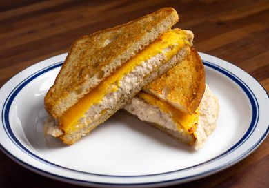 一个金枪鱼三明治放在盘子里，对角线切成两半，做成三角形;融化的黄色美国奶酪片放在奶油金枪鱼沙拉和烤得很好的面包上。