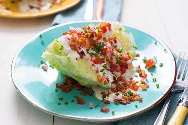 A loaded wedge salad on a light blue plate with a fork and knife off to the side