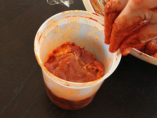 一只手在一夸脱大小的熟食容器中分层腌制猪肉。