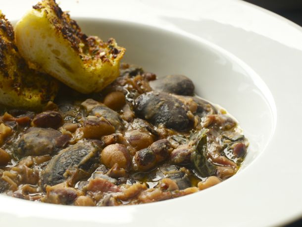 A bowl of ham, bean, and kale stew with two slices of toasted bread on the side.