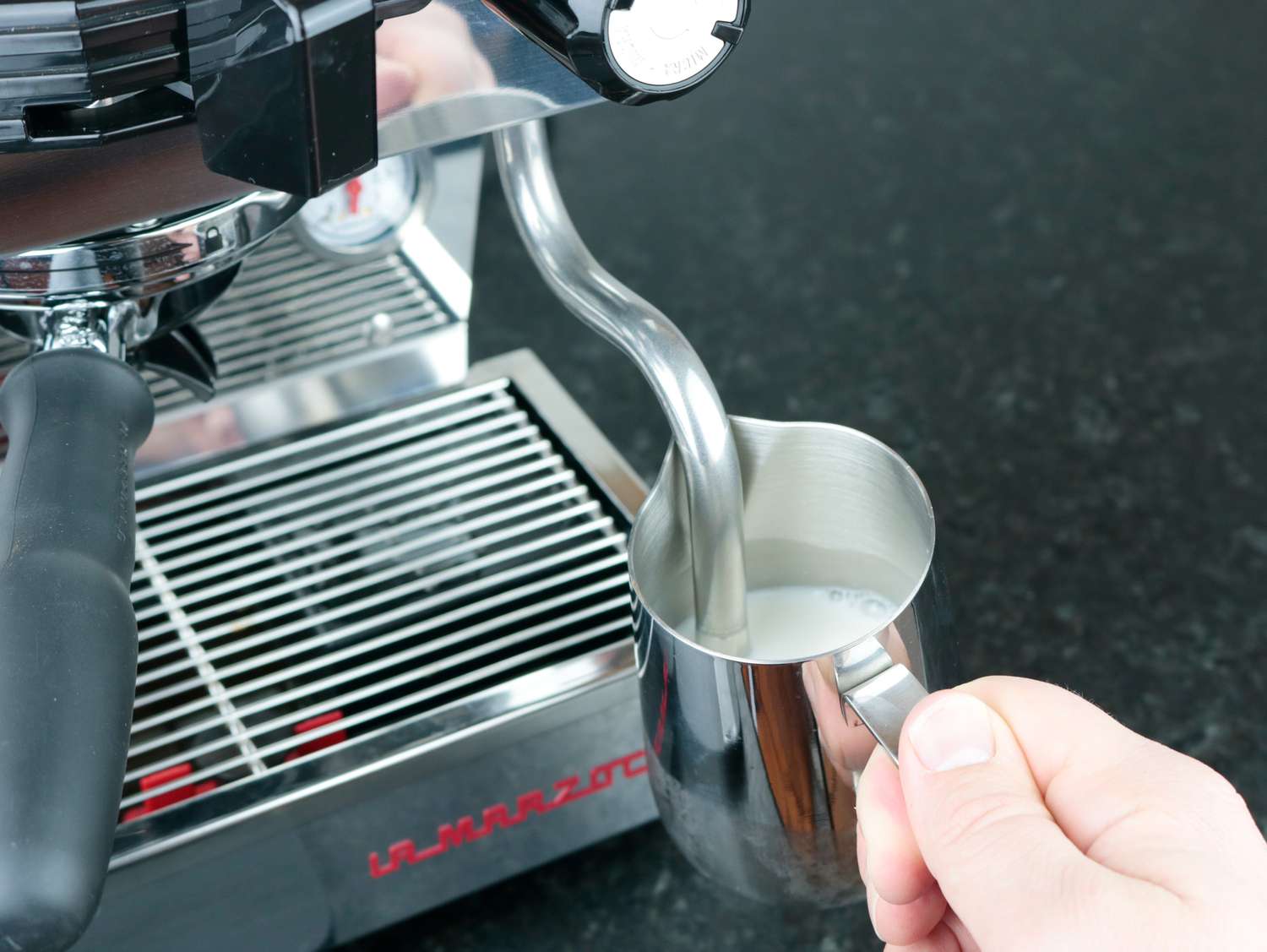 a steam wand being inserted in a pitcher of milk