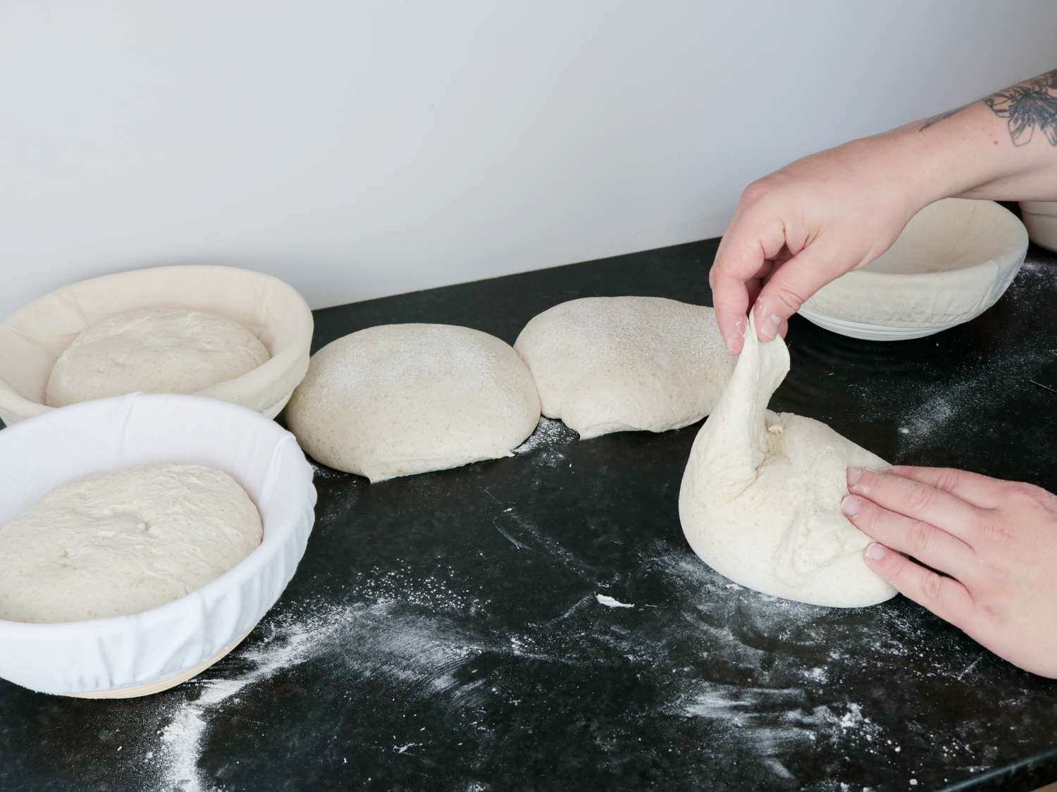 two proofing baskets with shaped bread dough in them on the left, a hand shaping bread dough into a round on the right