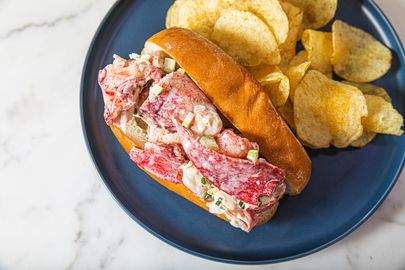 Overhead view of a stuffed lobster roll on a blue plate with potato chips