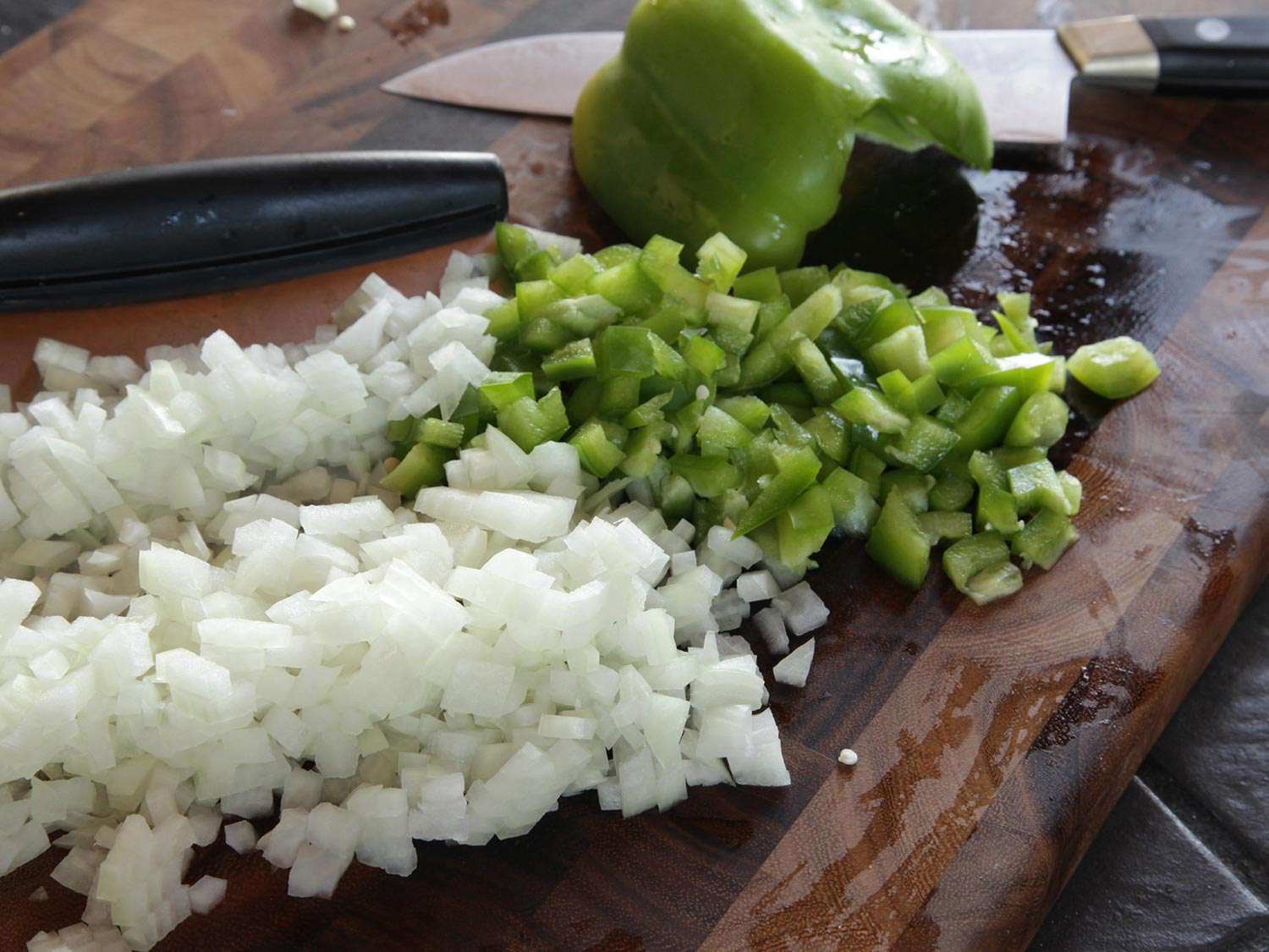 一堆切菜板上的洋葱丁和青椒丁，准备用刮刀转移到锅里。