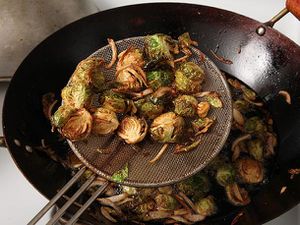 对半切开的球芽甘蓝和切片的青葱在锅里炸熟。一只金属蜘蛛正把一些蔬菜举在锅上。