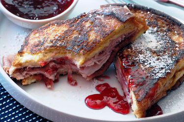 Plated Monte Cristo sandwich, partially dip.ped in red currant jelly with one half bitten into