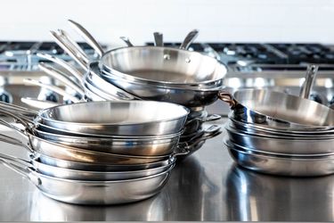 Stacks of stainless-steel skillets sit on a countertop.