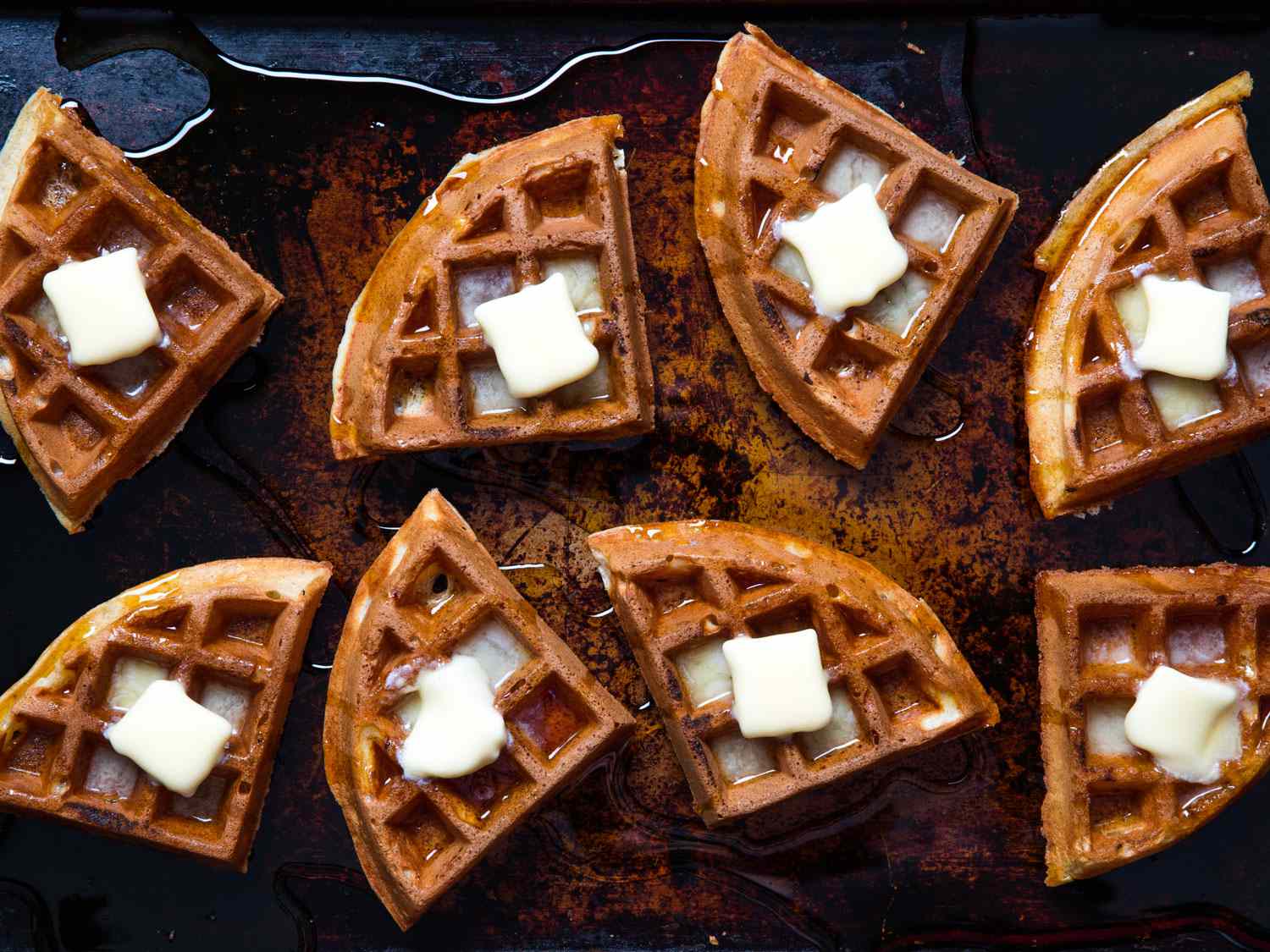 buttermilk waffle segments topped with butter and maple syrup on a baking sheet