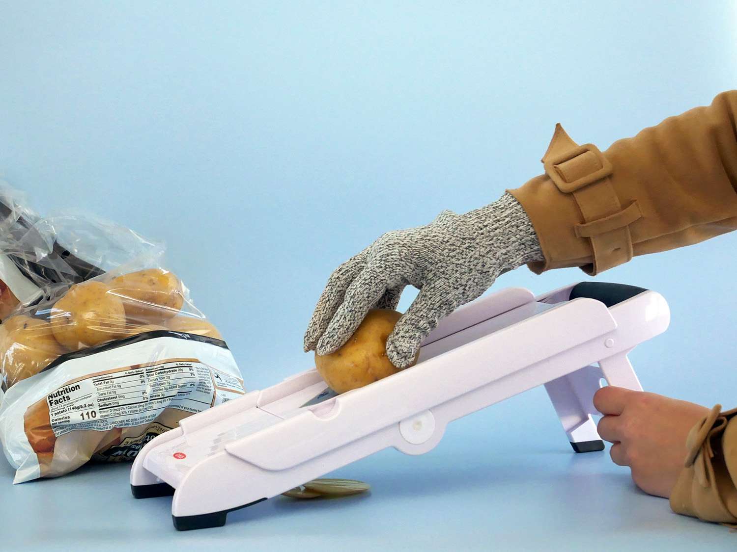 a hand with a cut-resistant glove sliding a potato over a mandoline