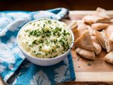 Bowl of puree potato topped with fresh herbs next to a pile of sliced pita bread