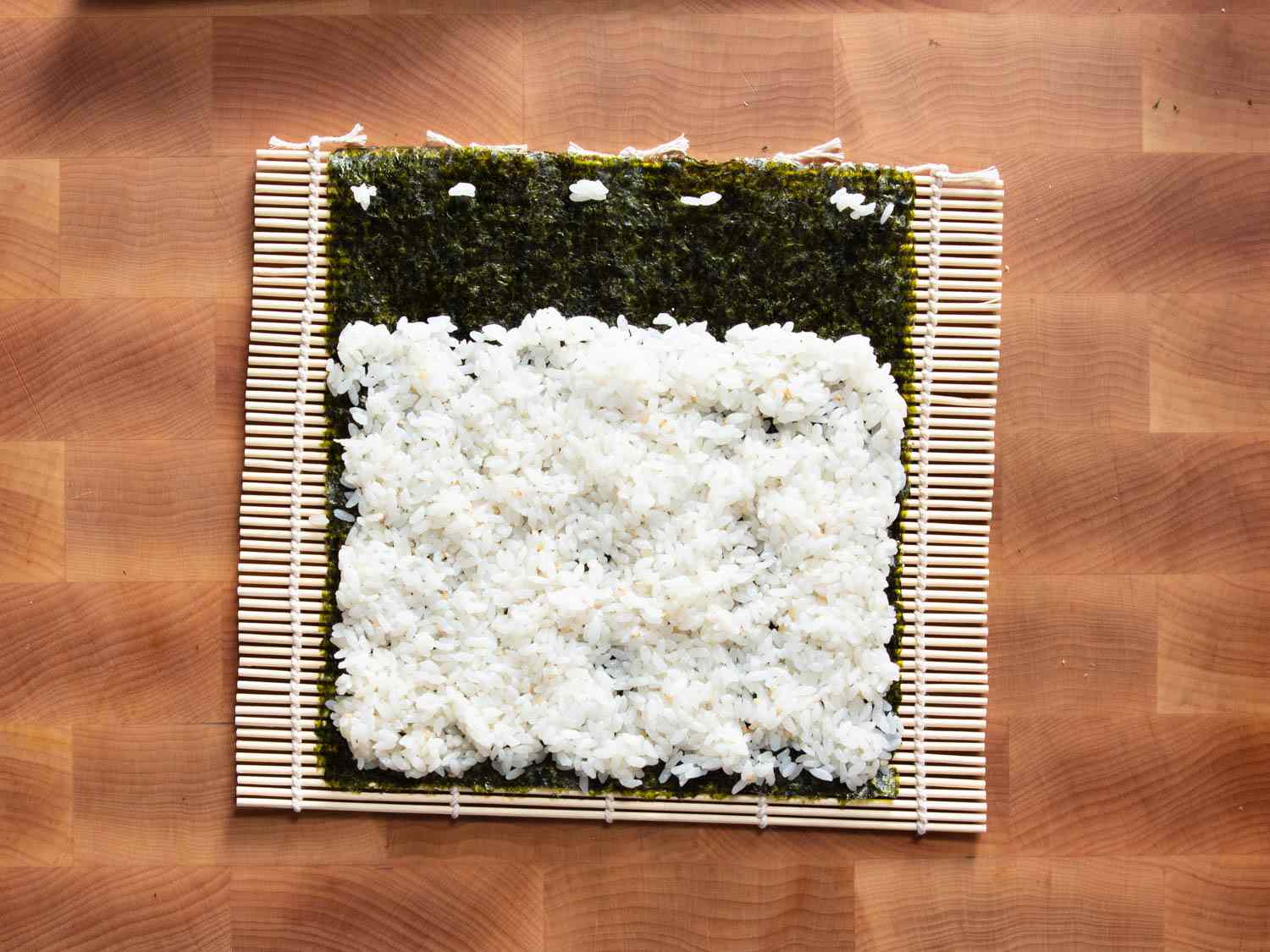 Overhead shot of sticky rice on seaweed resting on top of a bamboo rolling mat.