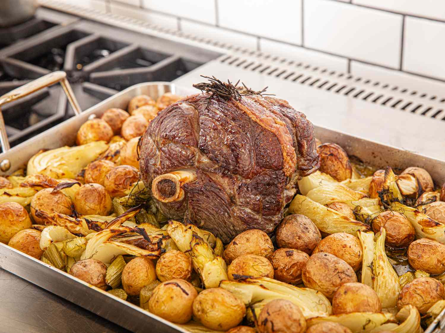 A cooked roast sitting atop browned potatoes and fennel in a roasting pan
