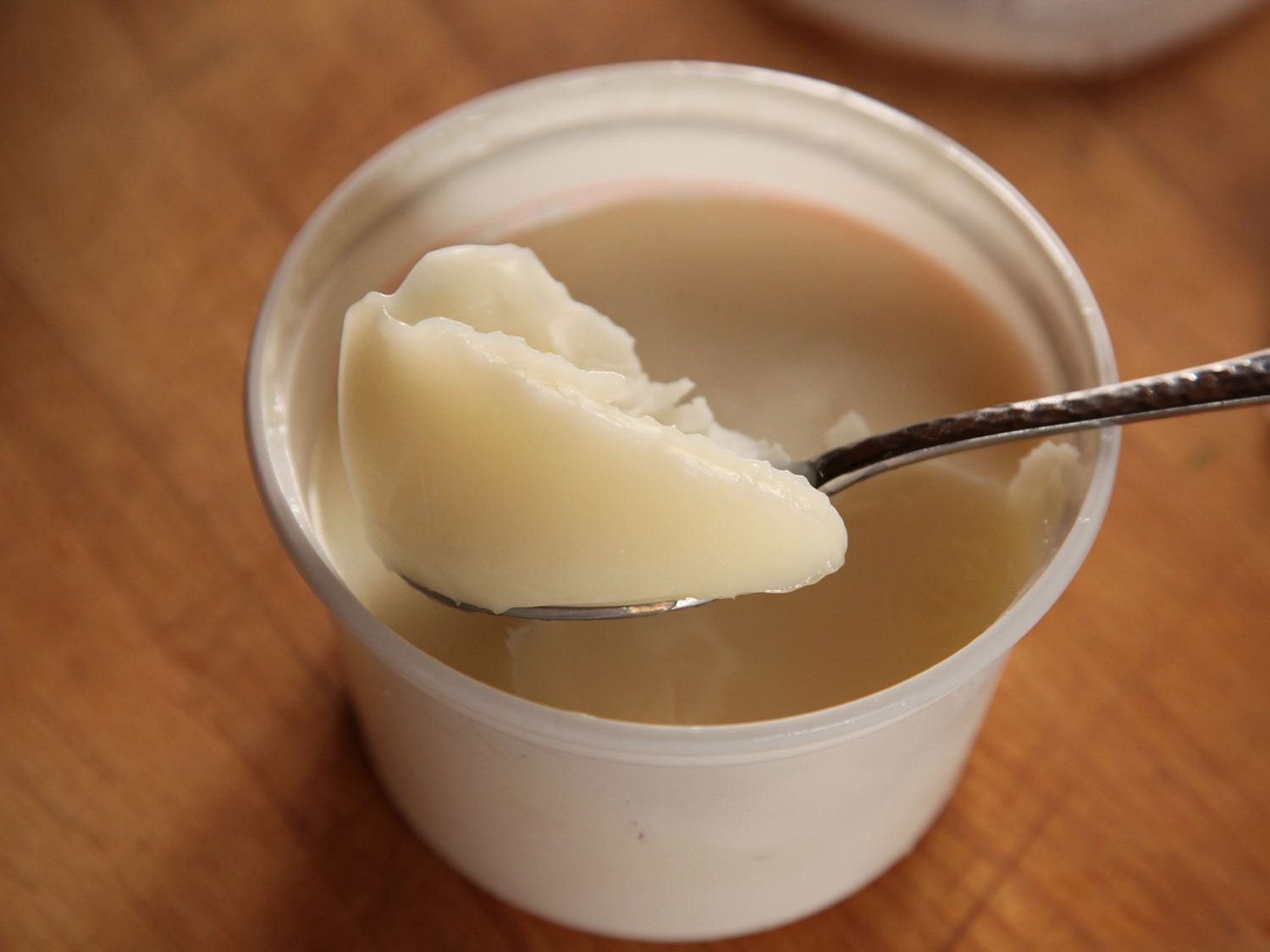 Scooping store-bought duck fat out of a plastic container for cassoulet.