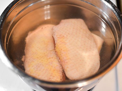 Duck breasts soaking on a metal mixing bowl filled with water.