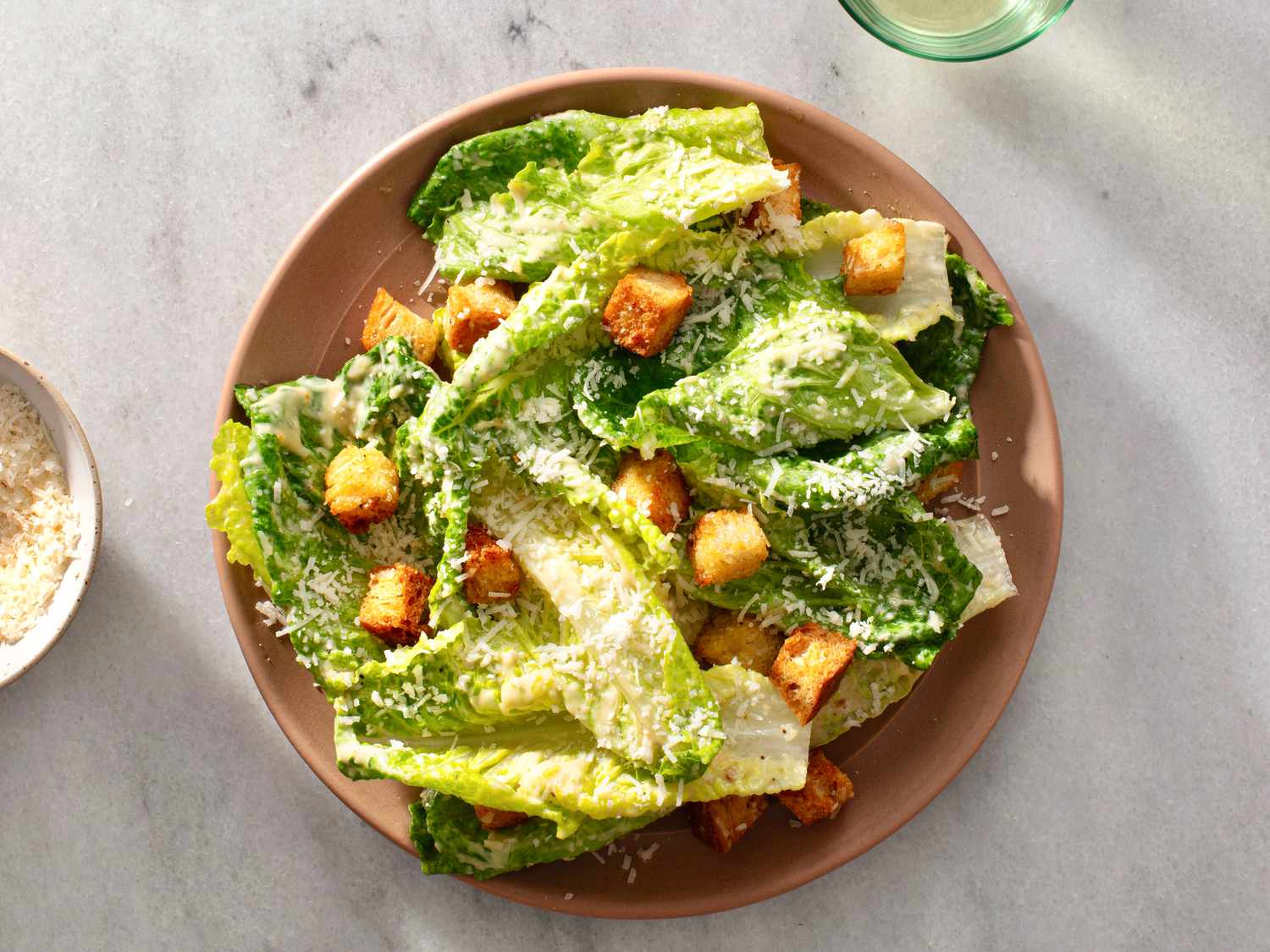 一个composed caesar salad in a ceramic bowl on a white stone background.