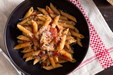 Overhead view of a black bowl of penne with arrabiata sauce.