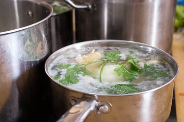 Three pots on a stove top. One smaller pot has chicken stock cooking in it.