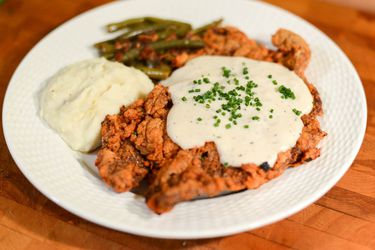 一盘有肉汁、土豆和蔬菜的炸鸡牛排